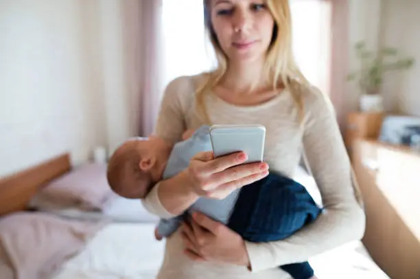 Photo of Mother with baby son in her arms and smartphone, texting