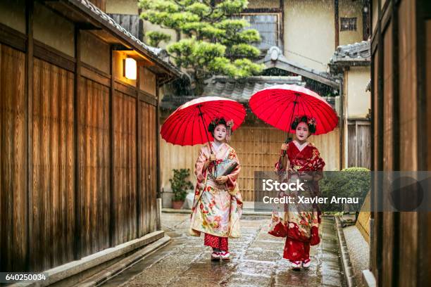 Geishas Holding Red Umbrellas During Rainy Season Stock Photo - Download Image Now - Kyoto City, Japan, Gion