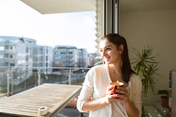 Woman relaxing on balcony holding cup of coffee or tea Beautiful young woman relaxing on balcony with city view holding cup of coffee or tea cardigan wales stock pictures, royalty-free photos & images