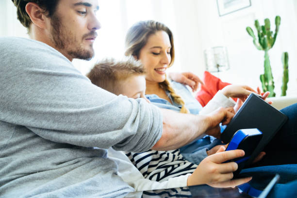 リビングルームで一緒に技術を使用して陽気な若い家族 - gamer watching tv adult couple ストックフォトと画像