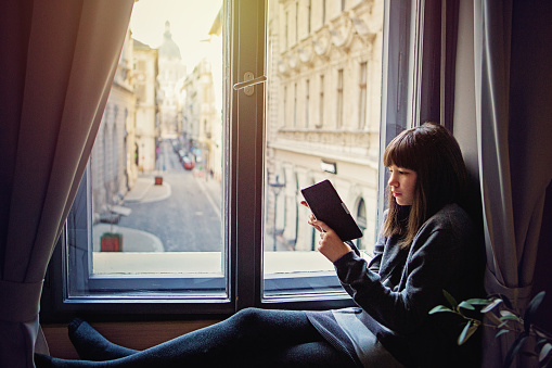 Young teenage girl is reading ebook on the window  with very nice city view