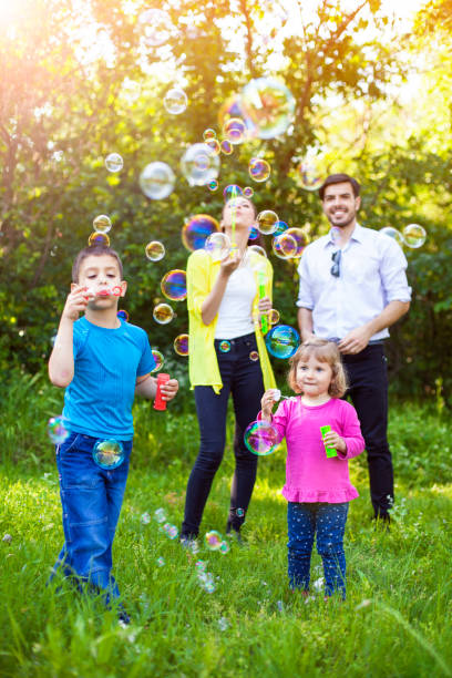 famille heureuse jouant avec des bulles de savon - bubble wand outdoors little boys mother photos et images de collection