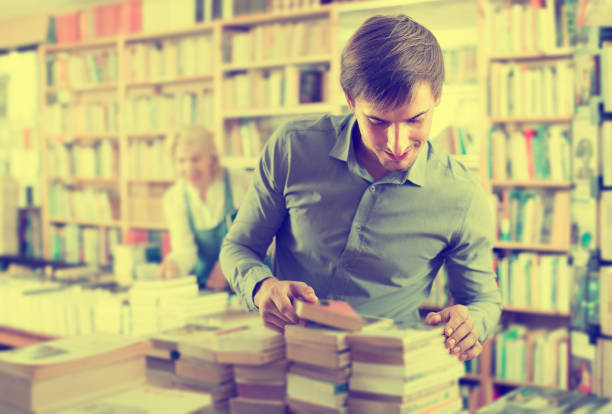 istock Young positive man picking new book on shelves 640271542