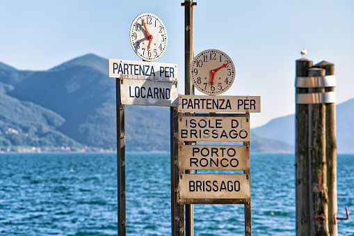 Clock at the Pier at the promenade in Ascona luxurious resort on Lake Maggiore, of Ticino canton in Switzerland. The letterings on the sings under the clocks are Names of towns and their piers on the Lake Maggiore, written In Italian.