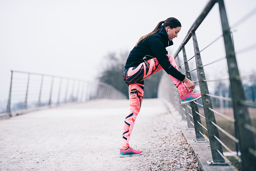Athlete young woman is tying her shoes on a bridge fence before training.