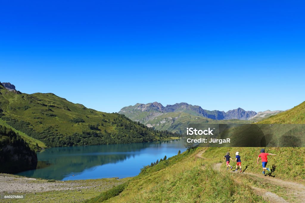 Kids Hiking in the Mountains Three boys are running on a hiking trail next to a beautiful mountain lake in Switzerland. The children are hiking in the mountains with their family. Family Stock Photo