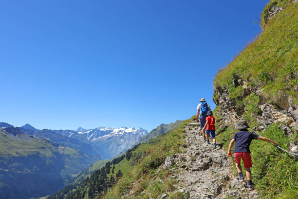 Adventurous Family Hiking in the Mountains Father and his two sons are hiking in the mountains in summer. The family is walking on an adventurous hiking trail at the edge of the mountain. This picture is taken on a Four Lakes Hike near Engelberg, Switzerland, but could be used for any mountain location. engelberg photos stock pictures, royalty-free photos & images