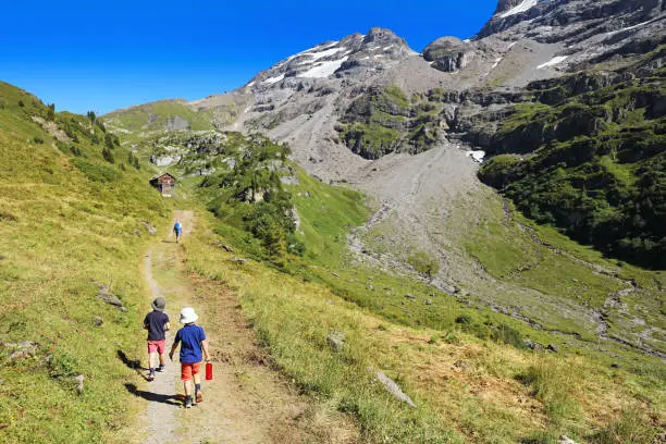 Two young boys and their dad are hiking in the mountains in summer. The family is walking on an adventurous Four Lakes hiking trail near Engelberg, Switzerland, but could be used for any generic mountain location.