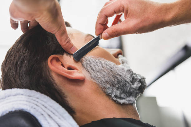 Skillful hairdresser shaving beard by blade Close up of barber arms getting rid of male stubble by special knife razor blade photos stock pictures, royalty-free photos & images
