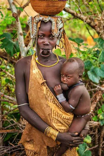 Woman from Mursi tribe breasfeeding her baby.  Mursi tribe are probably the last groups in Africa amongst whom it is still the norm for women to wear large pottery or wooden discs or ‘plates’ in their lower lips.http://bhphoto.pl/IS/ethiopia_380.jpg