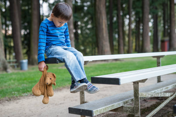 Young boy sitting by himself on bleachers and holding teddy bear.