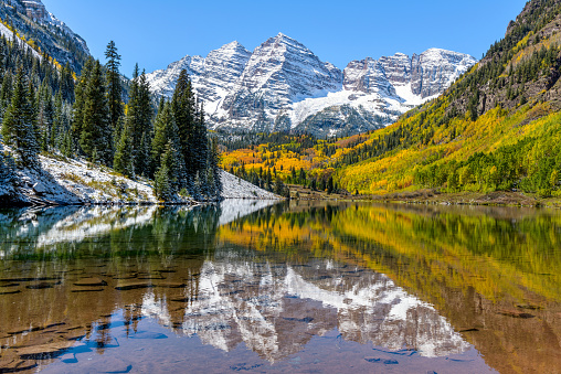 A wide-angle autumn midday view of snow coated Maroon Bells reflecting in crystal clear Maroon Lake, Aspen, Colorado, USA.
