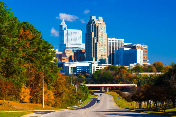 Raleigh Skyline in the distance with autumn colored trees Skyline of Raleigh in the distance with a road leading to it and autumn colored trees on the left side. raleigh north carolina stock pictures, royalty-free photos & images