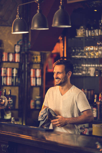 istock Smiling bartender at bar counter cleaning glass after work. 640303756