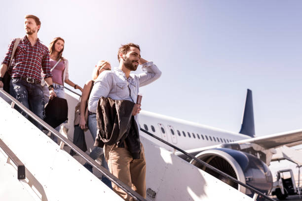 Group of young passengers disembarking the airplane. Below view of group of people leaving the plane by moving down the staircase. Focus is on man in the foreground. disembarking stock pictures, royalty-free photos & images