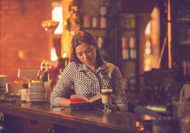 Young woman relaxing in a bar while reading a book at bar counter.