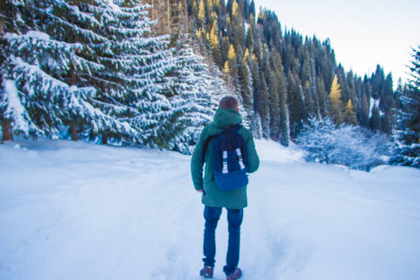 Young man with backpack is walking in winter mountains. Back view