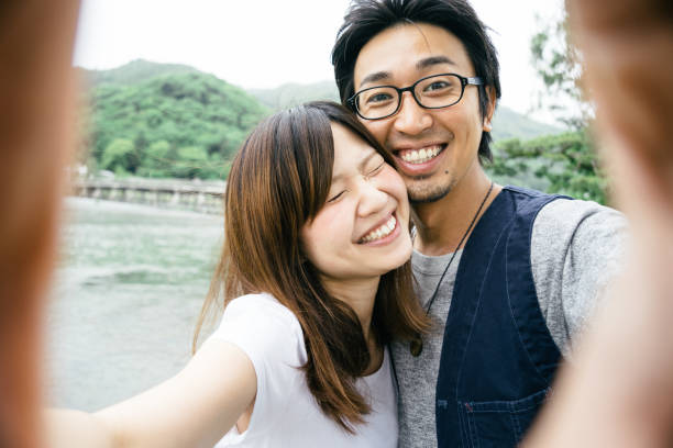 casal japonês alegre tirando selfie ao ar livre em um parque - togetsu kyo bridge - fotografias e filmes do acervo