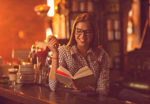 istock Smiling woman reading a book at bar counter. 640305368
