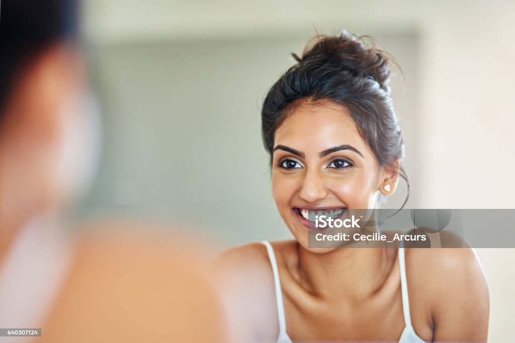 Good skincare definitely pays off Cropped of an attractive young woman looking at her face in the bathroom mirror Mirror - Object Stock Photo