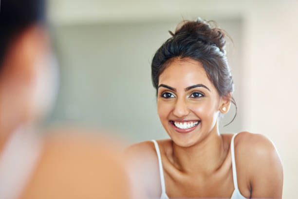 Good skincare definitely pays off Cropped of an attractive young woman looking at her face in the bathroom mirror mirror stock pictures, royalty-free photos & images