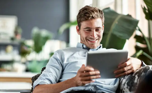 Shot of a happy young man using his tablet while relaxing on the couch at home