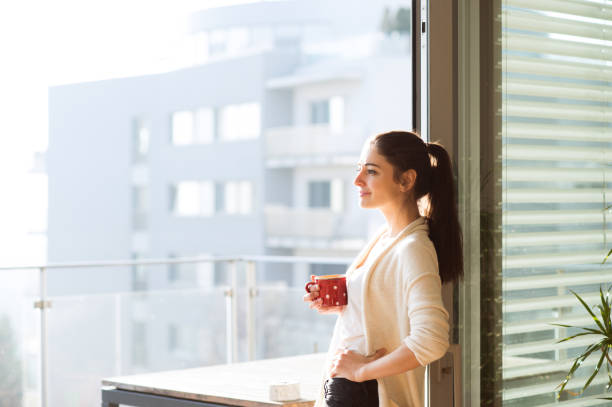 Woman relaxing on balcony holding cup of coffee or tea Beautiful young woman relaxing on balcony with city view holding cup of coffee or tea cardigan wales stock pictures, royalty-free photos & images