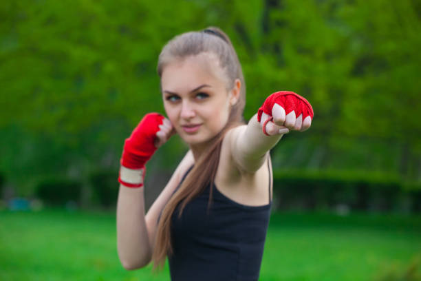 The girl the athlete, the boxer, in the park also gives the hand compressed in a fist forward with the reeled sports, red bandage. Preparation for training. Concept of sport and healthy lifestyle.