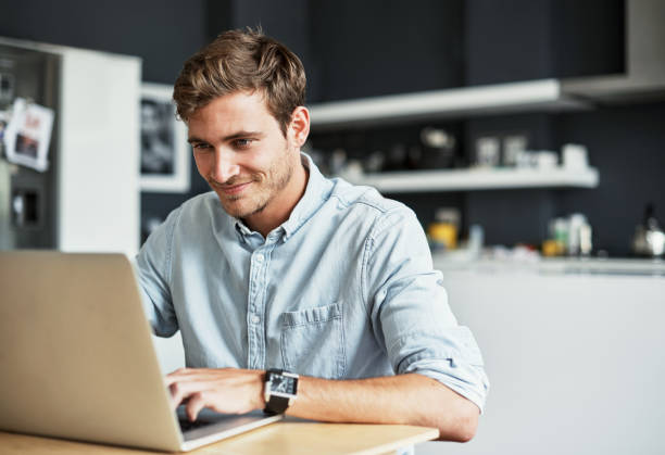 You can never watch too many cat videos Shot of a happy young man using his laptop while sitting in his kitchen at home using laptop home stock pictures, royalty-free photos & images