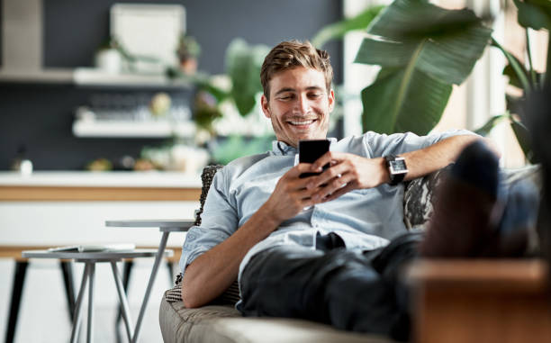Her messages always make him smile Shot of a happy young man using his cellphone while relaxing on the couch at home one young man only photos stock pictures, royalty-free photos & images