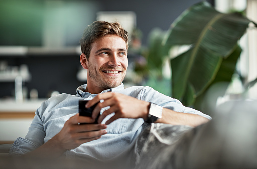 Shot of a happy young man using his cellphone while relaxing on the couch at home