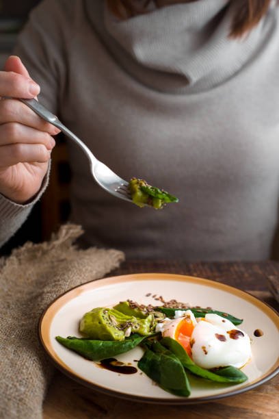 istock Woman eating poached egg with avocado cream vertical 640313256