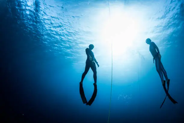 Two free divers, man and woman, ascending from the depth