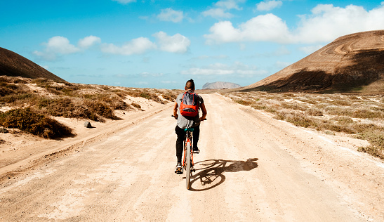 a young man seen from behind riding a bike in a dirty road in La Graciosa, Canary Islands, Spain
