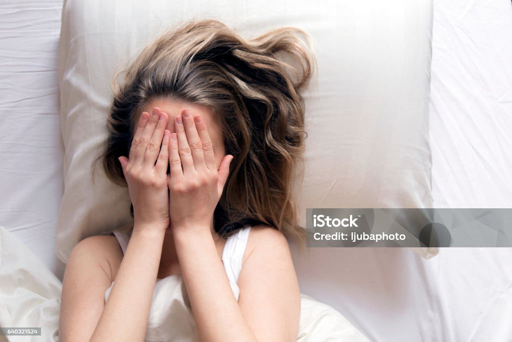 She is covering her head with her hands in bed - Royalty-free Slapeloosheid Stockfoto