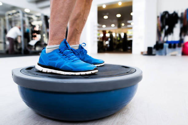 Unrecognizable senior man in gym standing on bosu balance ball Close up of legs of senior man in gym standing on bosu balance ball and exercising as part of bodybuilding training balance stock pictures, royalty-free photos & images