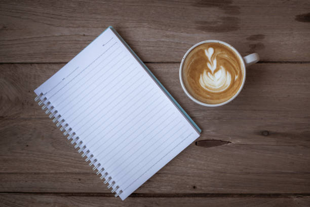 Close up shot of an unrecognizable woman writing something in the notebook while having a cup of coffee and a piece of cake.
