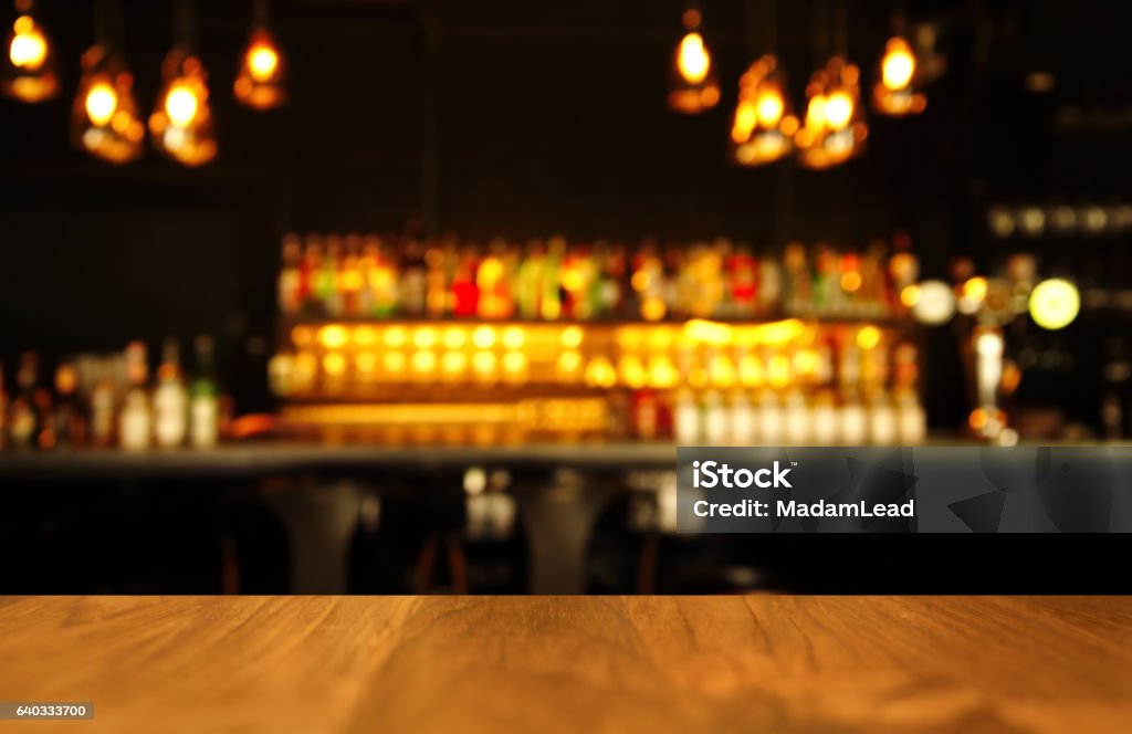 wood table with blur light of lamp and bar wood table with blur light of lamp and bar with bottle abstract bacgournd Alcohol - Drink Stock Photo