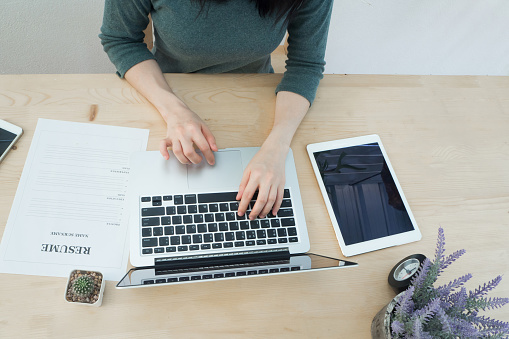 Office table with businessman's hand typing on keyboard ,resume information and blank screen on tablet, Purple lavender flower on pot. find job concept. View from above office table.