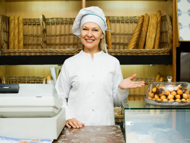 Mature woman posing in bakery with baguettes Mature woman posing in bakery with baguettes and buns old candy store stock pictures, royalty-free photos & images