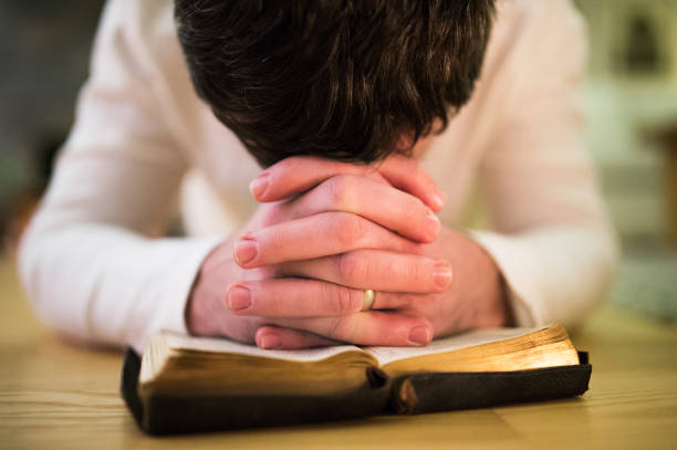 istock Unrecognizable man praying, kneeling on the floor, hands on Bibl 640342754