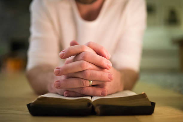 istock Unrecognizable man praying, kneeling on the floor, hands on Bibl 640342914