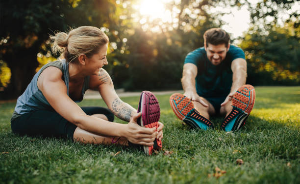 Young caucasian couple exercising in park Happy young man and woman stretching in the park. Smiling caucasian couple exercising in morning. warm up exercise stock pictures, royalty-free photos & images