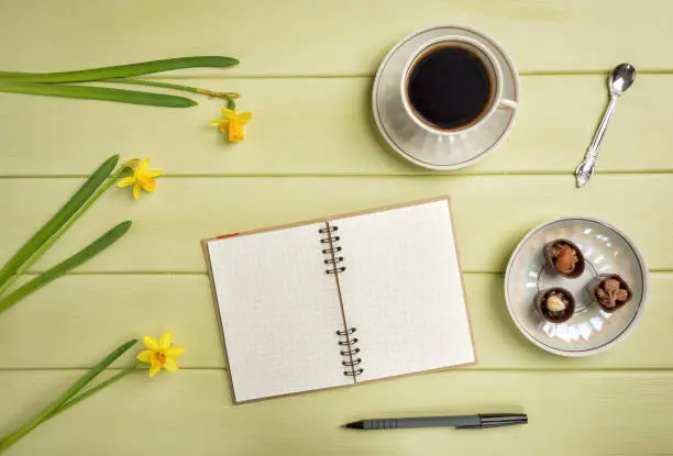 Notebook, a pen, cup of coffee and flowers on a wooden background. Top view. Copy space.
