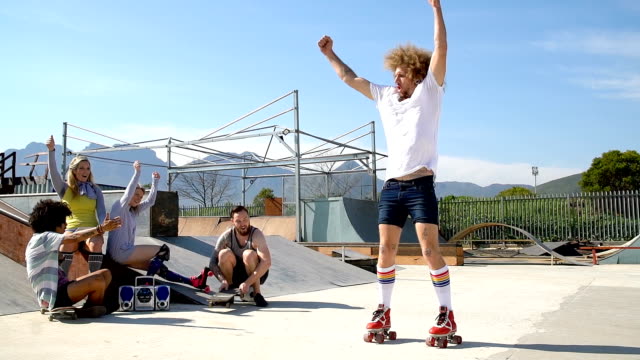 Hipster friends hanging out watching man roller skating in sunny skate park