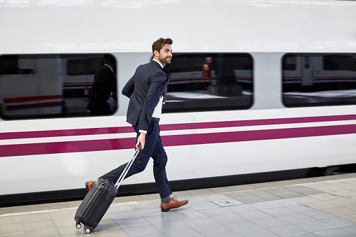 Full length of businessman running with wheeled luggage. Male professional is at railroad station. He is wearing suit.