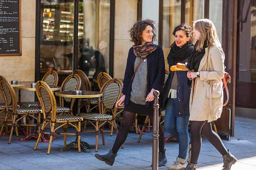 Group of young women friends walking past a typical French cafe in Paris early in the morning