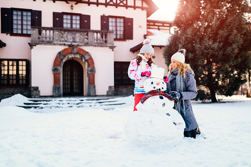 Mother and daughter having fun outdoors at winter. They are making snowman.