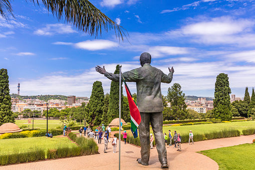 Pretoria, South Africa - January 29, 2017: Nelson Mandela statue at the Union Buildings facing Pretoria city, with the South African flag next to him seen from the rear. Tourists seen below taking pictures of this landmark statue. A UNESCO world heritage site.