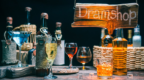 Wineglasses with sparkling wine and cocktails on counter of dramshop or liquor shop. Orange light beam on the wood sign and the counter